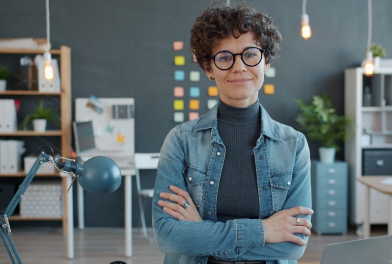 A woman with glasses smiles in an office.