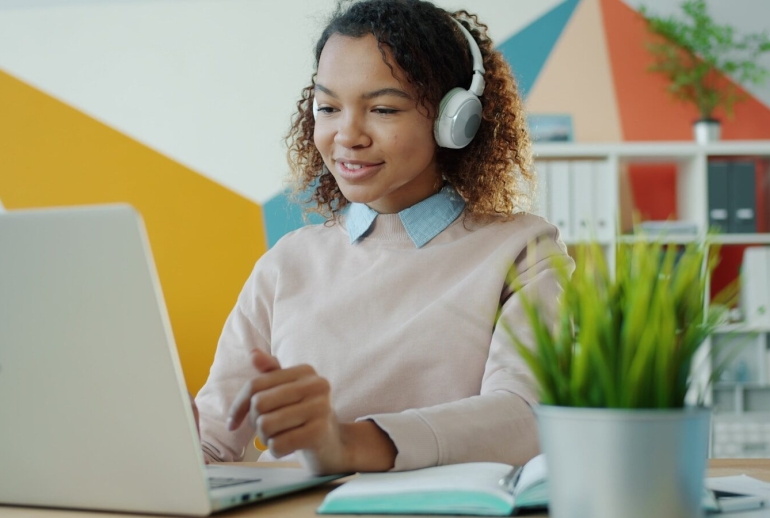 Young woman wearing headphones works on laptop.